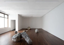 A contemporary art gallery with sculptures, a dark wooden floor and white walls.