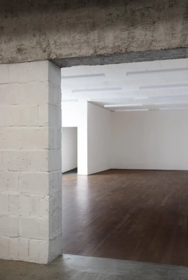 An art gallery with white concrete walls, a dark wooden floor and a large concrete beam.