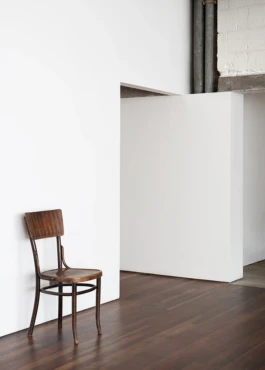 A room with white walls, dark wooden floors and a wooden chair.