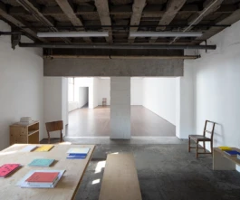 A workspace with a concrete floor, ceiling, white painted walls, and coloured books on a table.