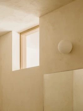 An angled photograph of lime plastered walls, a small circular wall light and windows.