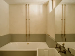 A bathroom with textured, cream and green walls and exposed copper pipework.