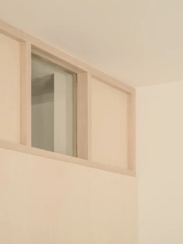 A cropped photograph of walls with bespoke wooden joinery details and a small square window.