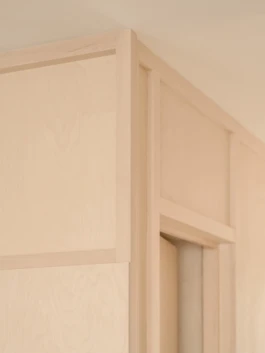 The corner of a bespoke, light coloured timber wall and an open door.