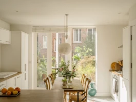 A kitchen with a dining table in front of a large window with planting and flowers.