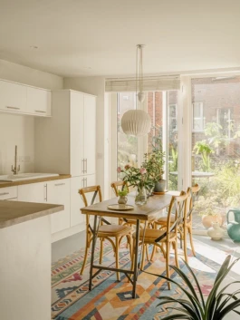 A kitchen with a wooden dining table and a colourful patterned rug on the floor.
