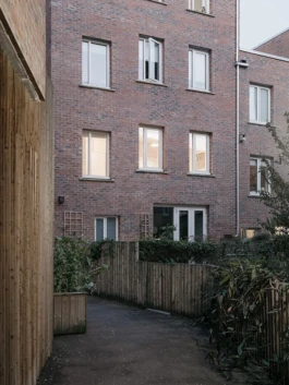 A tall red brick house at dusk, with lots of windows with lights on.