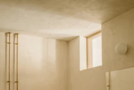 An angled photograph of lime plastered walls, a small circular wall light and windows.