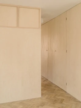 An angled photograph of an interior with parquet flooring and birch plywood panelling on the walls.