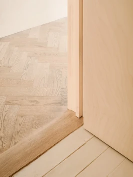 A zoom photograph of the junction between oak flooring, ceramic floor tiles and birch plywood walls.