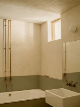 A bathroom with textured cream and green walls, and sunlight coming through a square window.