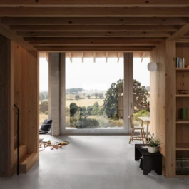 A room with a timber ceiling and a large rectangular window with views across a hillside.