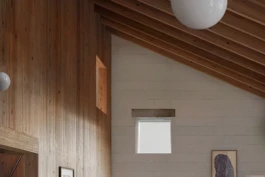 A double height room with timber rafters, painted concrete blockwork walls and square windows.