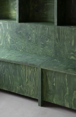 A zoom photograph of a dark green stained timber bench seat on a light grey floor.