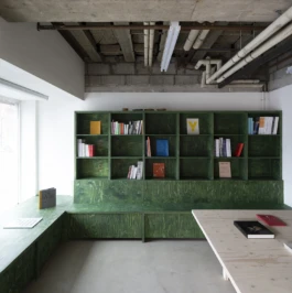 A bookshop with a concrete floor and ceiling, and dark green bookshelf.