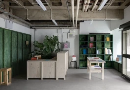 A bookshop interior with a pale wood reception desk, display tables and green bookshelves.