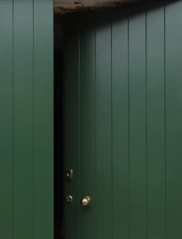 A zoom view of a green, vertical panelled timber door that is slightly open.