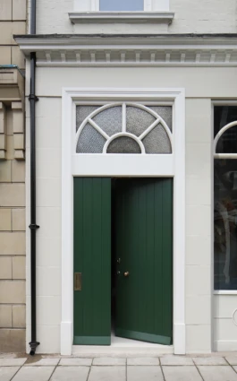 A green, vertical panelled timber door with an ornate arched clerestory window above the entrance.