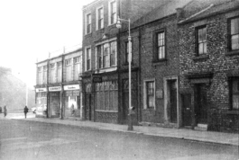 A historic photograph taken from a road with a pub and terraced houses to each side.