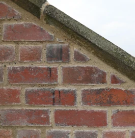 A close, zoom view of a historic, red brick wall with an angled coping stone.