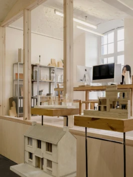 Architectural models in a studio space with computers in the background.