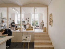 A studio with architectural models and timber stairs leading up to a mezzanine office space.