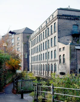 Looking along a footpath towards historic mill buildings constructed from stone with green window frames.