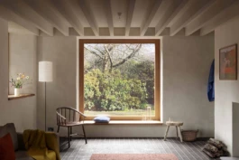A home interior with timber ceiling beams and a large window with views of trees outside.