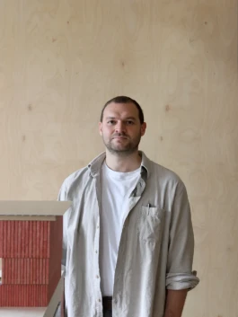 Photograph of staff member next to plywood wall and architectural model
