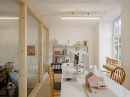 An office space with windows to the sides, lots of natural daylight, computers and architectural models.