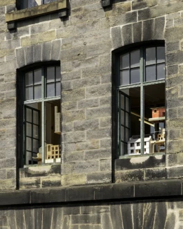 A view outside a building with large stone walls and architectural models on display in the windows.
