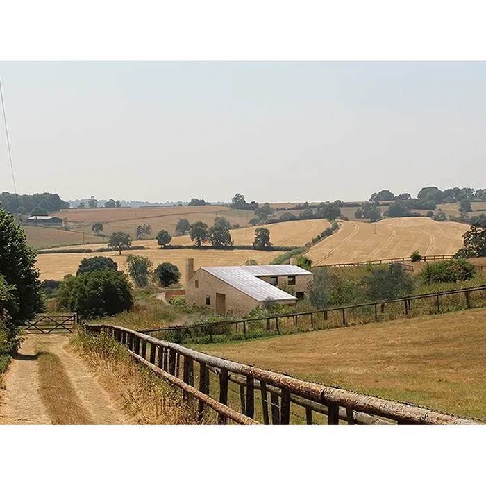 Topo Architects — A house with a chimney on a sunny hillside surrounded by fields and trees.