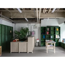 A bookshop interior with a pale wood reception desk, display tables and green bookshelves. 