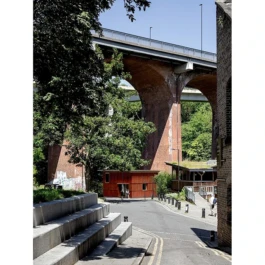 A red timber building below a large, arched, vehicular bridge. 