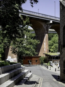 A red timber building below a large, arched, vehicular bridge.